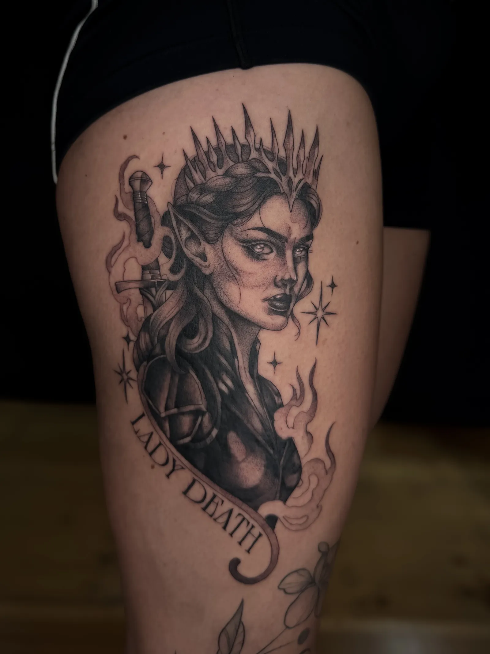 Lady Death from the A Court of Thorns and Roses books on the thigh: a crowned woman with a dagger above a banner reading Lady Death