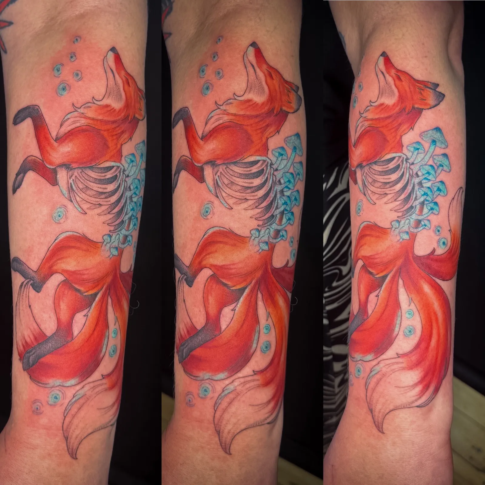Colour tattoo of a decaying red fox on the outer forearm, its ribcage showing, with blue mushrooms growing from it