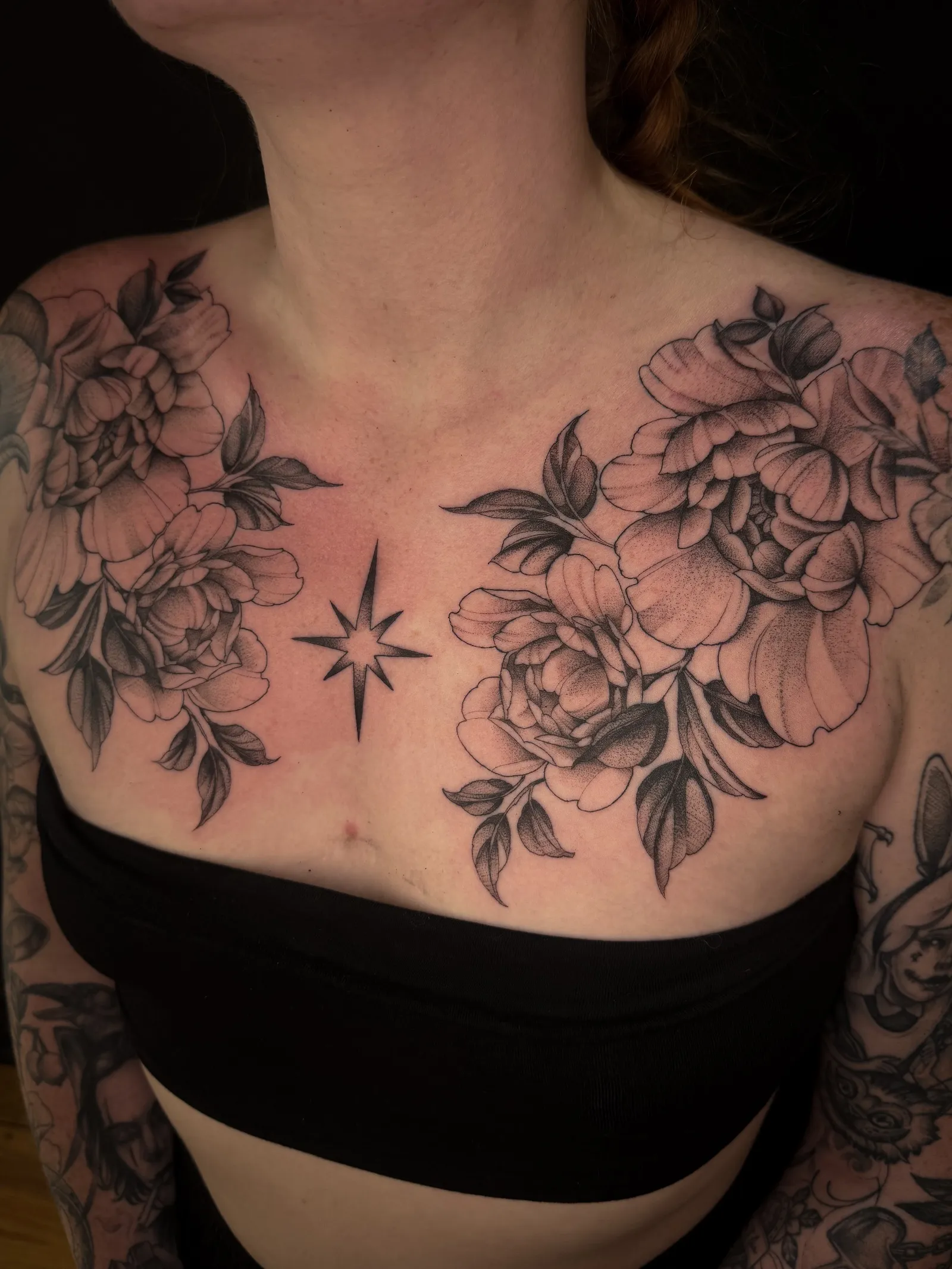Fine line peonies across both sides of the chest, with a small eight-pointed star in the centre
