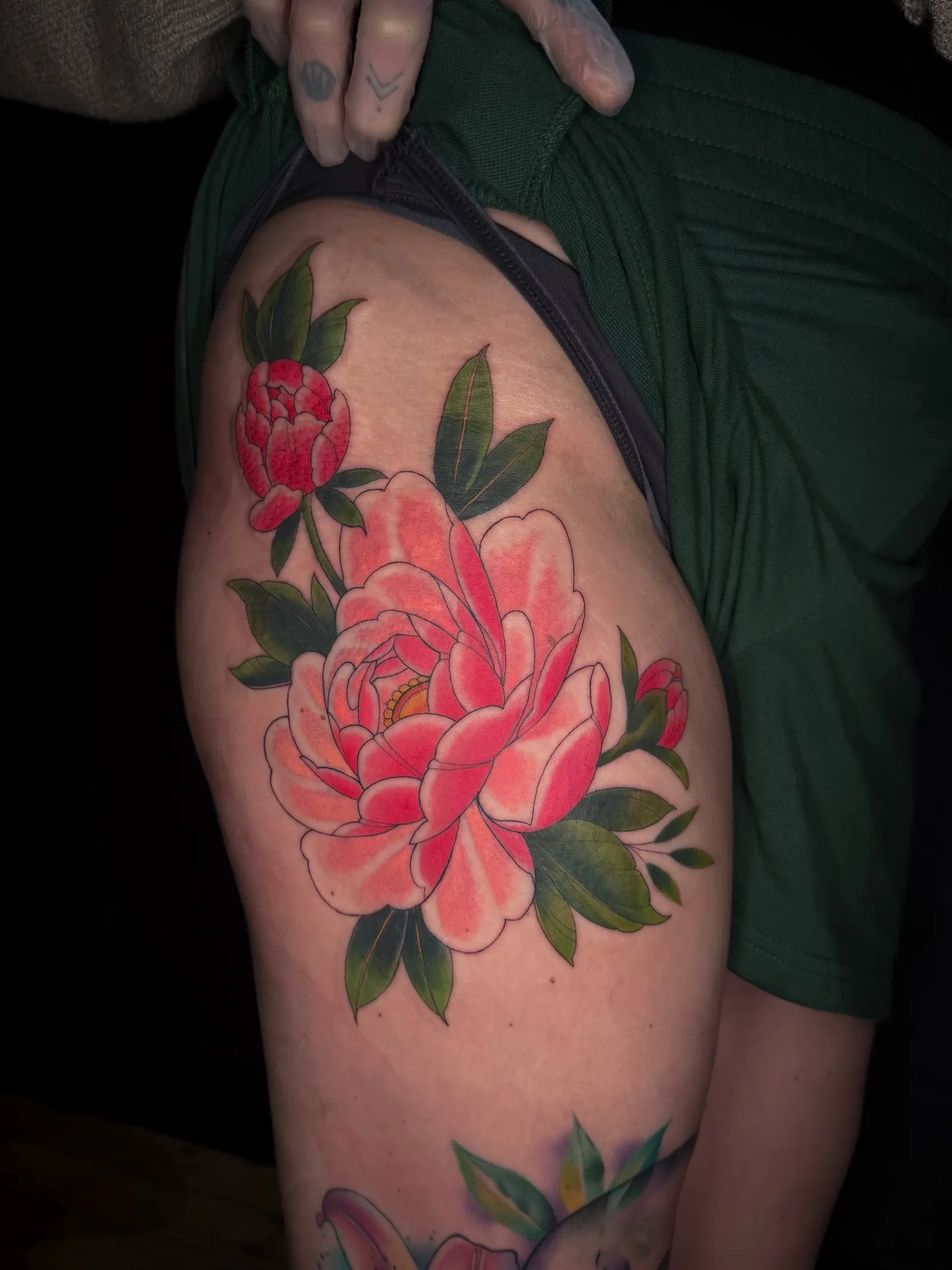 Neo-Japanese colour tattoo of bright pink and red peonies with green leaves on the outer thigh