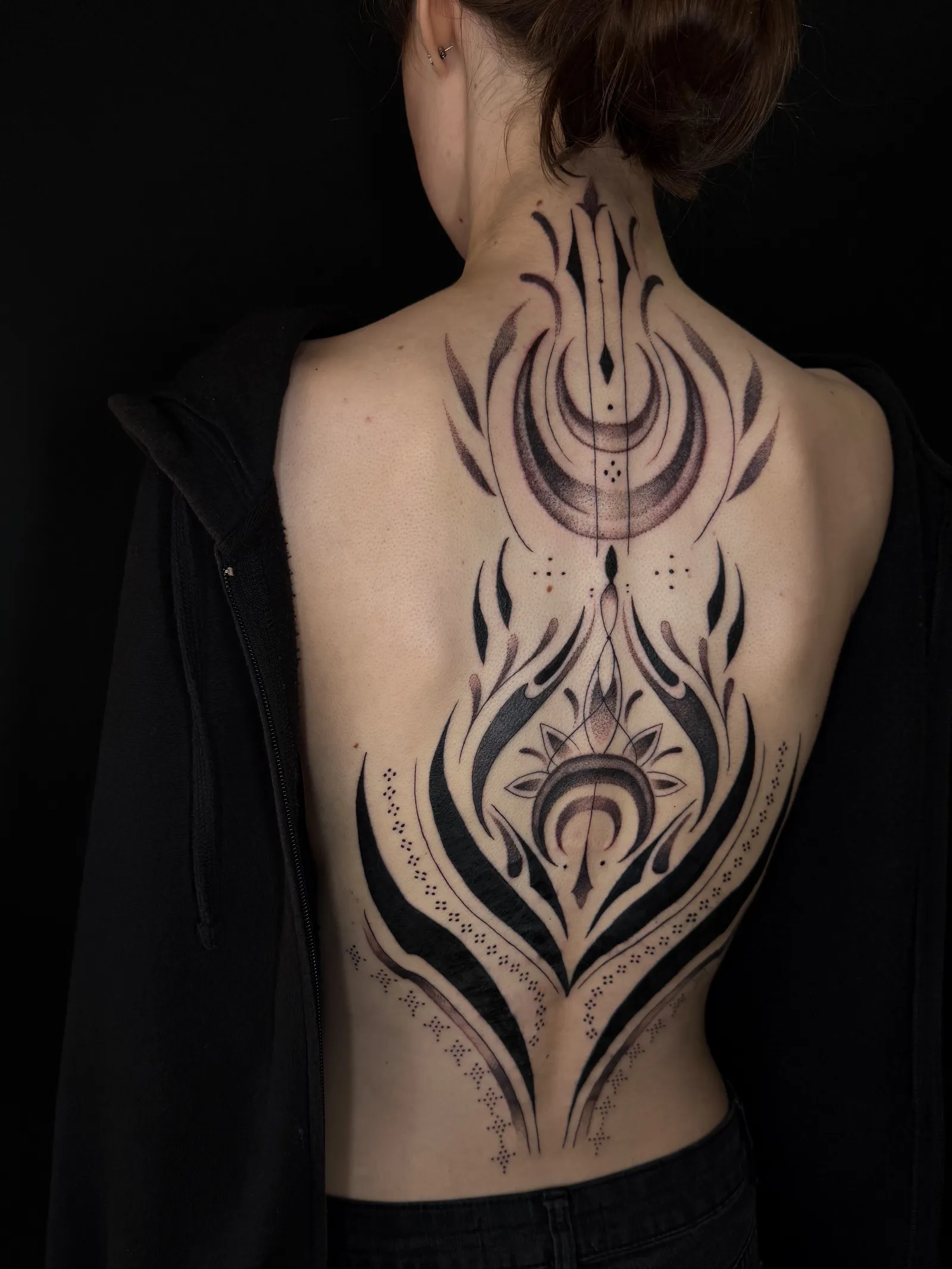 Ornamental blackwork down the spine: crescent moons, a lotus, bold flowing shapes and fine dotwork